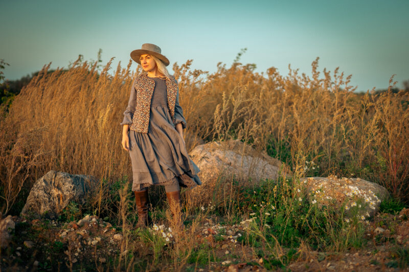 Lady standing in the nature in blowing wind in grey dress and flower printed vest